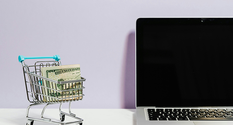 Image showing a miniature shopping cart full of cash next to a laptop.