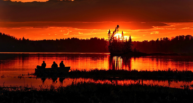 Image featuring a sunset with a boat in the lake, carrying three men.